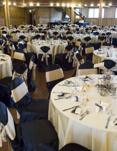 Banquet hall arranged with round tables, black chair covers, and gold bows
