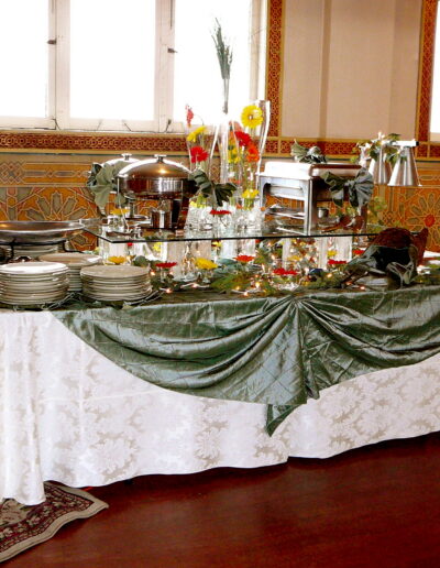 Buffet table with silver chafing dishes, green linens, and bright floral arrangements