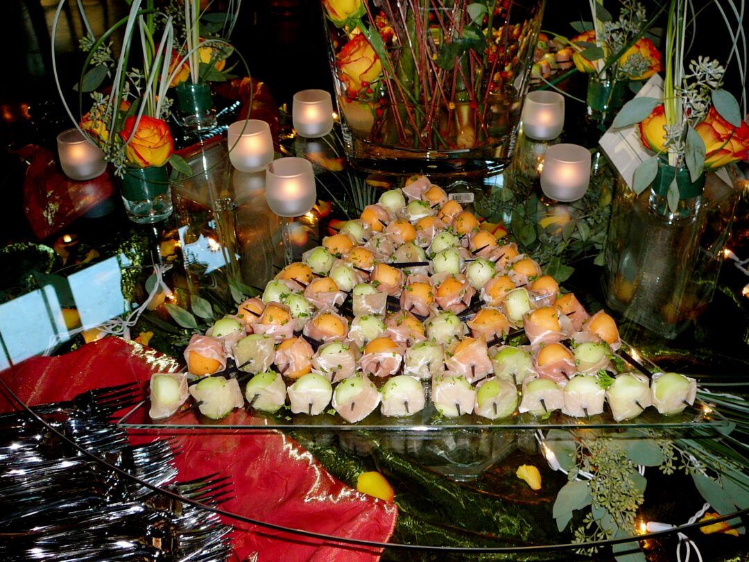 Prosciutto-wrapped melon bites displayed with yellow roses and candles