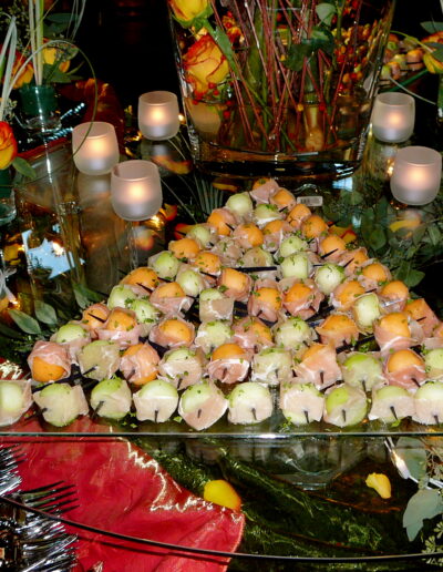 Prosciutto-wrapped melon bites displayed with yellow roses and candles