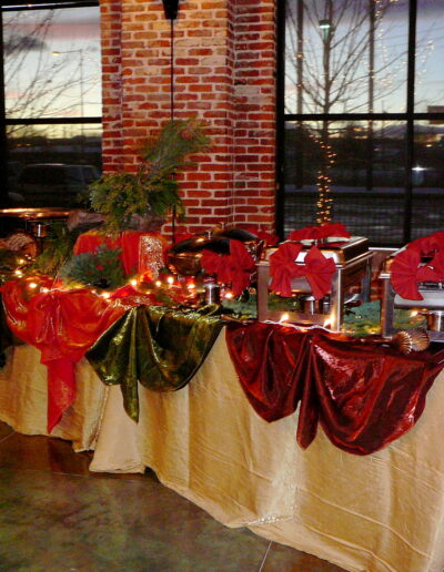 Buffet station with red-and-green draping, chafing dishes, and string lights