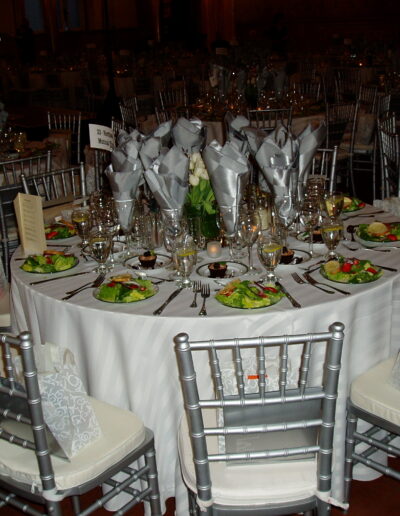 Formal banquet table set with silver chairs, folded napkins, salads, and glassware