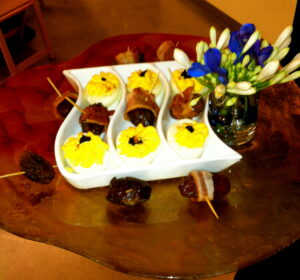 Tray of deviled eggs and bacon-wrapped dates with blue-and-white flowers